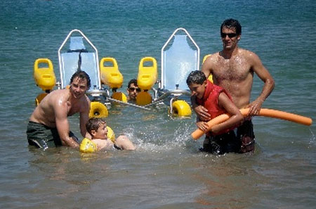 Dos niños con diversidad funcional y tres adultos jugando en el mar