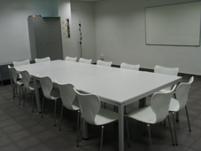 Fotografa de una sala blanca con una mesa rodeada de sillas y una pizarra