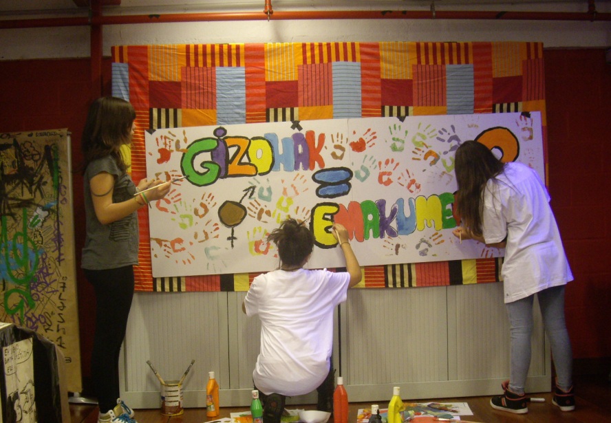 Tres jvenes pintan una pancarta con el texto 'Gizonak = Emakumeak' 