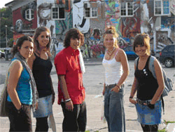five teenager pose in front of a house full of graffiti
