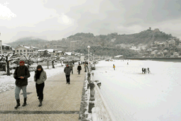 Fotografa con la playa Ondarreta cubierta de nieve y personas caminando por el paseo